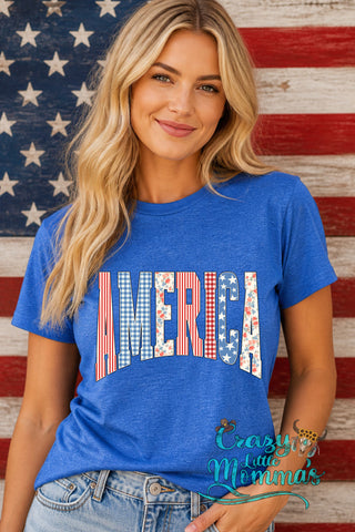 A woman in a blue "America" tee with patriotic patterns on the letters, standing against an American flag.