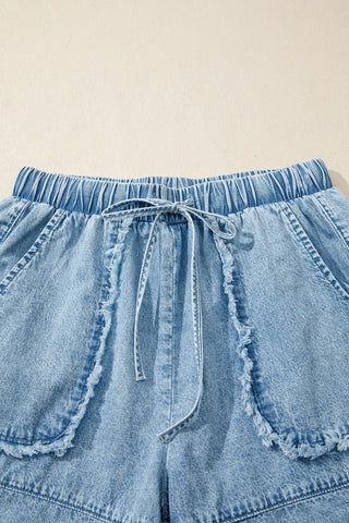 Close-up of light wash Canyon Frayed Hem Shorts with an elastic waist, drawstring, and distressed denim.