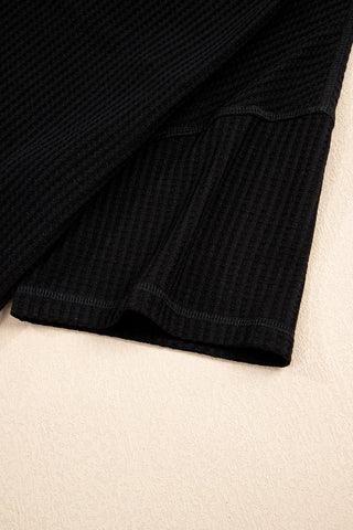 Close-up of a black casual waffle knit top, showing the textured fabric and stitched hem.