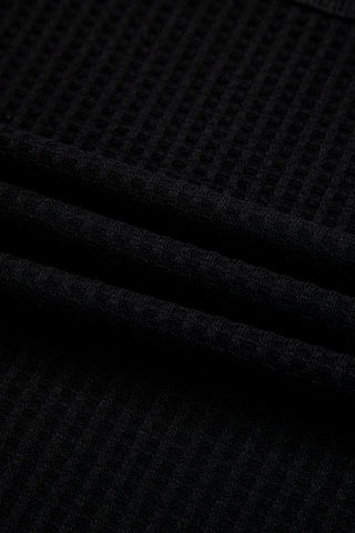 Close-up of a black casual waffle knit top, showing the textured fabric and soft folds.