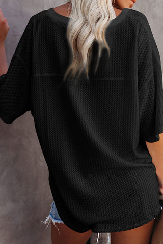 Back view of a woman wearing a black Canyon Waffle Knit Top with short sleeves and a relaxed fit.