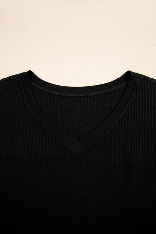 Close-up of a black casual waffle knit top with a V-neckline, showcasing the textured fabric.