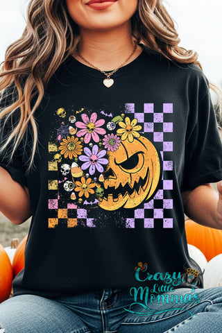 A woman wears a black checkered Halloween floral tee with a pumpkin, flowers, skulls, and candy corn design.