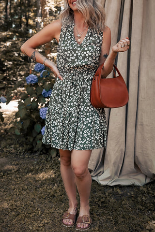 Woman in a sleeveless olive floral mini dress with a ruffled neckline, drawstring waist, and tiered skirt.