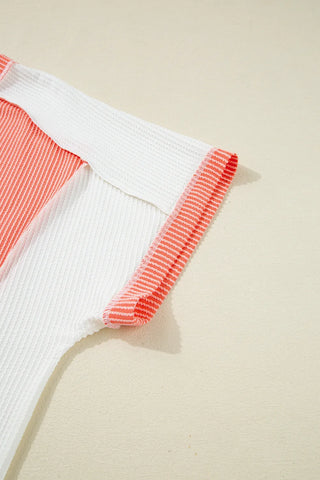 Close-up of a coral ribbed panel top with white panels and striped coral trim on the sleeve.