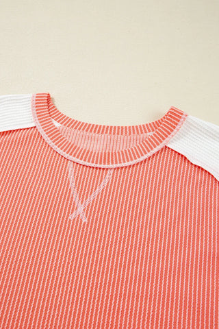 Close-up of a coral ribbed panel top with white ribbed sleeves and a V-stitch detail at the neckline.