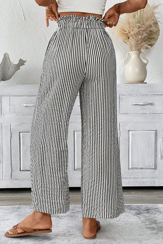Woman wearing black and white striped paperbag waist pants with a ruffled high waist and wide legs.