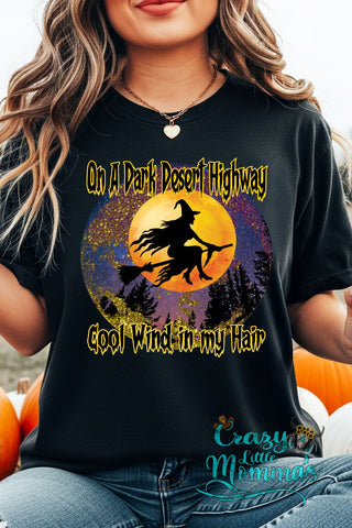 Woman wearing a black Dark Highway Witch Tee with a witch flying on a broomstick against a full moon.
