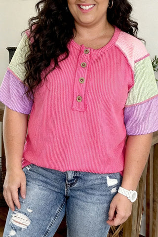 A woman models a pink patchwork henley top with green and purple sleeves and distressed jeans.
