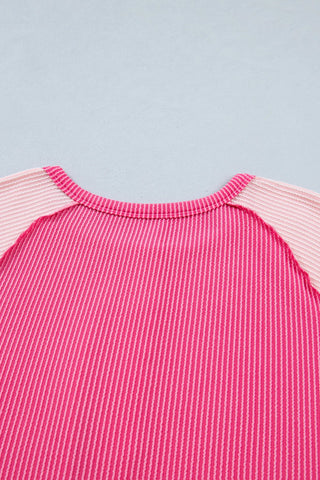 Close-up of a pink patchwork henley top with ribbed texture and light pink raglan sleeves.