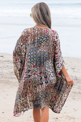 Woman from behind wearing a bohemian floral kimono with a desert bloom pattern on a sandy beach.