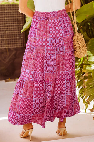 A woman wears a Desert Bloom Maxi Skirt, featuring a bohemian patchwork design in shades of pink and purple.