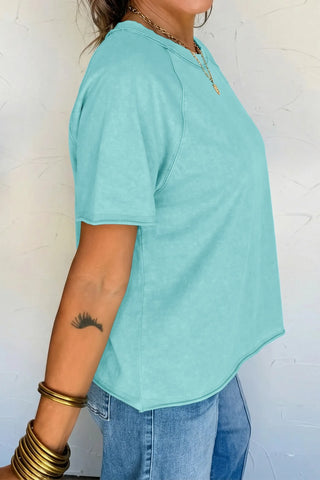 Side view of a woman wearing a Desert Sky Raglan Tee in a washed teal color with blue jeans.