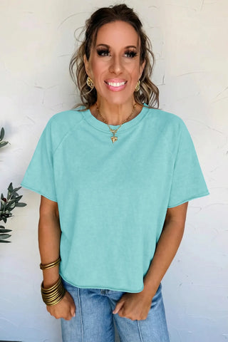 A smiling woman models a Desert Sky Raglan Tee, a washed teal raglan tee with short sleeves.