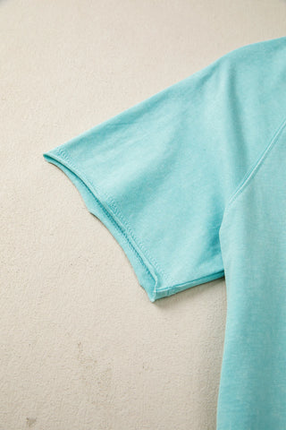 Close-up of a washed teal raglan tee sleeve, showing the fabric texture and stitching against a light background.