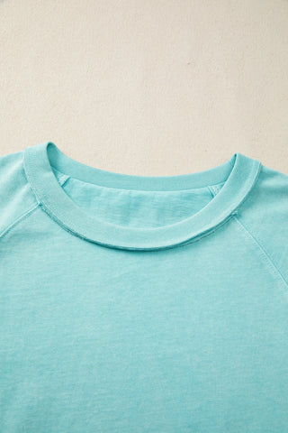 Close-up of a Desert Sky Raglan Tee, showing the washed teal fabric and ribbed neckline.