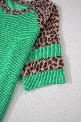Close-up of a green ribbed top with leopard print raglan sleeves and striped cuffs.