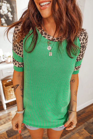A woman wears a green ribbed top with leopard print raglan sleeves, smiling.