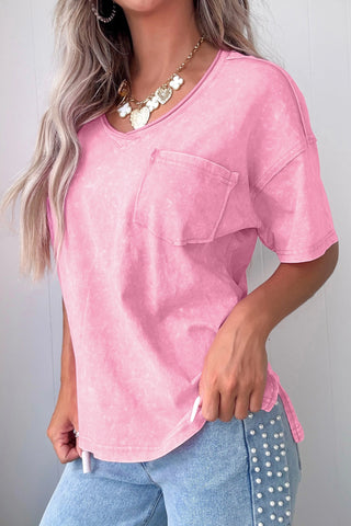 A woman wears a dusty rose acid wash V-neck top with a front pocket, paired with light wash jeans.