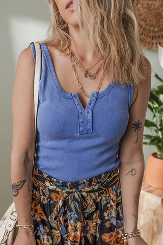 Woman wearing a dusty blue ribbed Henley tank top with a button placket, paired with a floral skirt.
