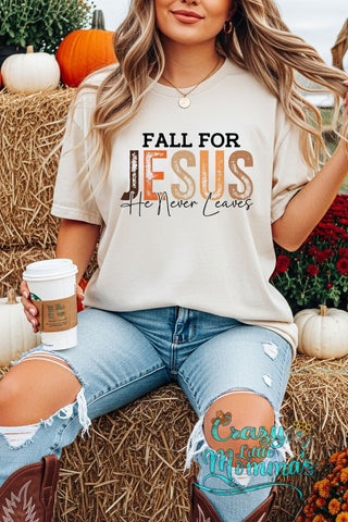 Woman in a Fall Christian graphic tee with "Fall for Jesus He Never Leaves" text, sitting on hay bales.