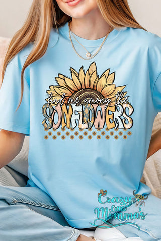 A woman wearing a light blue "Find Me Among Sunflowers" tee with a large sunflower graphic.