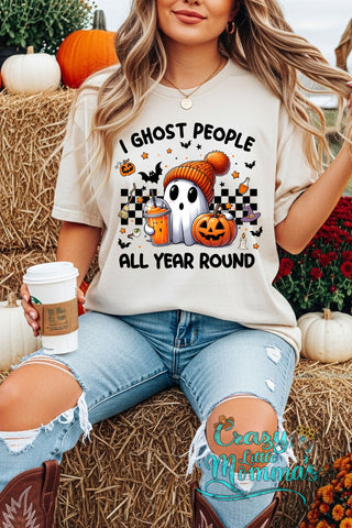 Woman in a "I Ghost People All Year Round" graphic tee with a ghost, pumpkin, and checkered pattern.