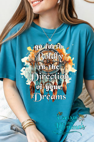 Woman wearing a teal "Go Forth Boldly" tee with an inspirational dreamcatcher compass graphic.