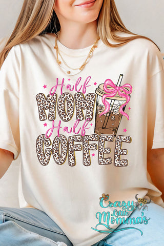 A woman wears a cream Half Mom Half Coffee tee with leopard print text and an iced coffee with a pink bow.