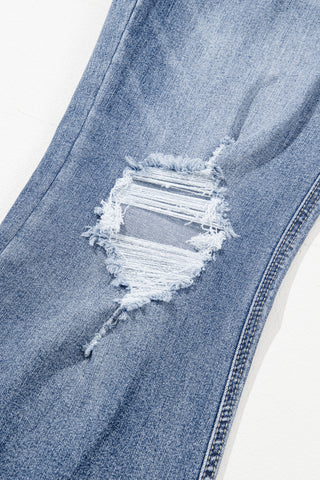 Close-up of light wash Western distressed flare jeans with a large rip and frayed edges on the thigh.
