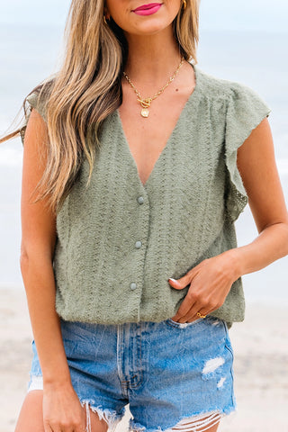 Close-up of a woman wearing a sage ruffle button top with a textured knit and distressed denim shorts.