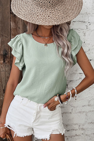 Woman in a straw hat wearing a light green Prairie Ruffle Blouse with white shorts and beaded bracelets.