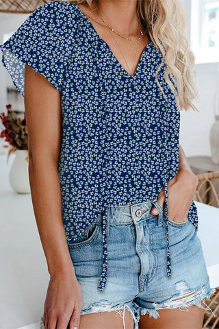 Woman wearing a navy floral flutter top with a v-neckline, paired with distressed denim shorts.