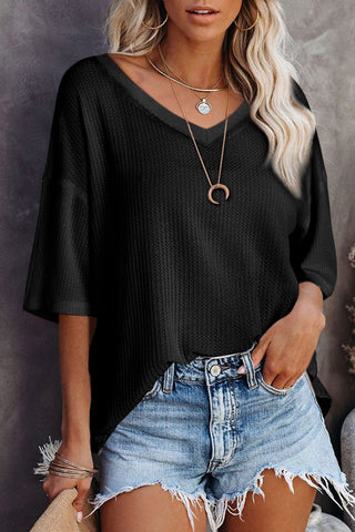 Woman wearing a black Canyon Waffle Knit Top with a V-neck, paired with denim shorts.