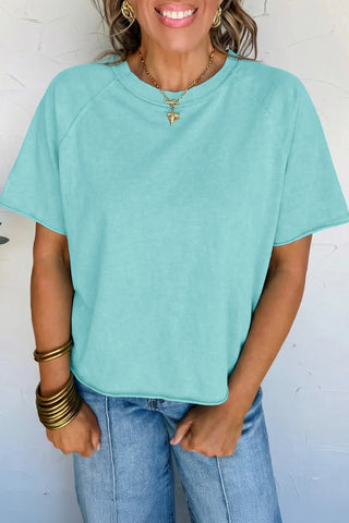 A woman models a Desert Sky Raglan Tee, a washed teal raglan tee, with light wash jeans.