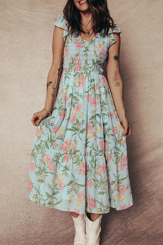 Woman smiling, wearing a light blue smocked floral prairie midi dress with pink and yellow flowers.