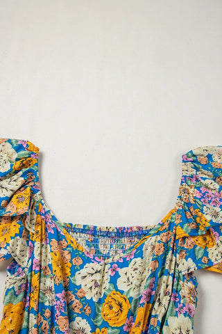 Close-up of a blue floral smocked jumpsuit with yellow, pink, and white flowers, and ruffled sleeves.