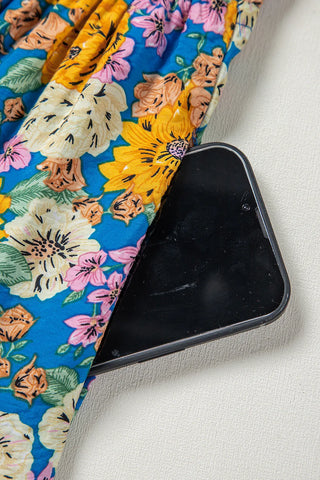 Close-up of a smartphone tucked into the pocket of the blue floral smocked jumpsuit.