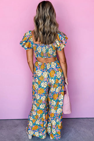 Back view of a woman wearing a blue floral smocked jumpsuit with yellow, pink, and white flowers.