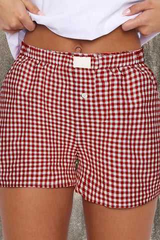 Close-up of a person wearing red and white gingham shorts with an elastic waistband and a single white button.