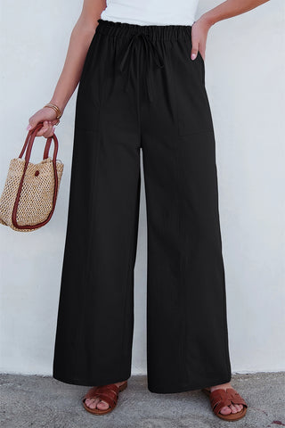 A woman wears Midnight Prairie Wide Pants, featuring a drawstring waist and relaxed black palazzo pant style.