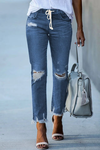 Woman wearing Ranch Hand Distressed Jeans with ripped knees, frayed hems, and a drawstring waist.