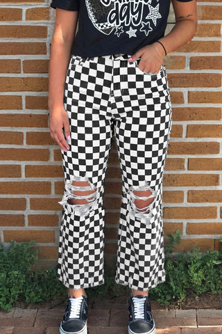 A person wearing black and white checkerboard distressed jeans with ripped knees and frayed hems.