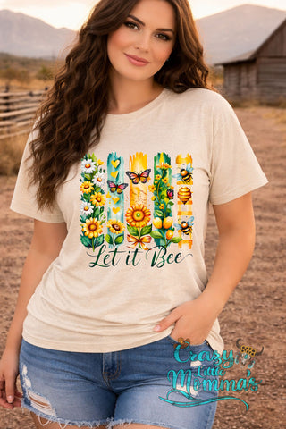 A woman models a beige "Let it Bee" tee with a colorful graphic of flowers, butterflies, and bees.