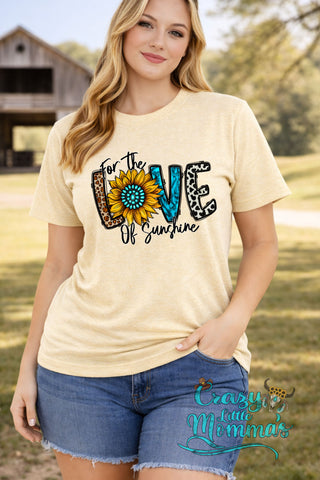 Woman in a Love of Sunshine Tee, featuring a sunflower and leopard print text, paired with denim shorts.