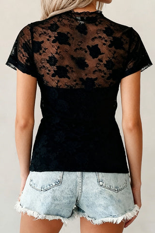 Back view of a woman wearing a black Midnight Bloom Lace Top with sheer floral lace and short sleeves.