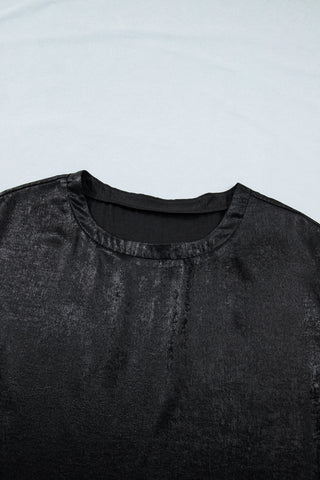 Close-up of a black shimmer draped blouse with a textured, metallic sheen and a simple round neckline.