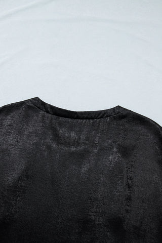 Close-up of a black shimmer draped blouse, showing the textured fabric and neckline against a light background.