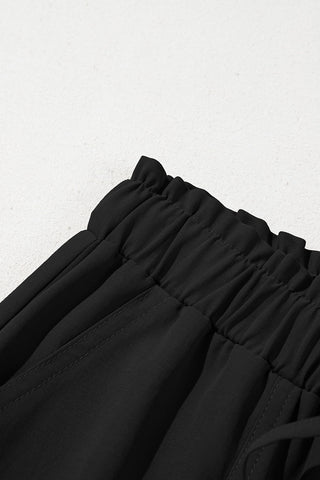 Close-up of the elastic, ruffled waistband and pockets of black wide-leg pants.
