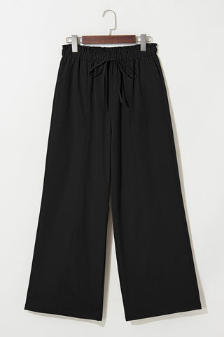 Black wide-leg pants with an elastic waist and drawstring, hanging on a hanger against a white background.